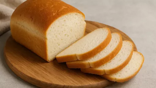 Felii de pâine albă de grâu pe o planșetă de lemn, lângă o franzelă